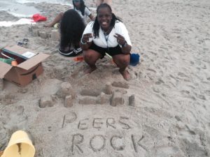 A PeerFest attendee at the beach poses for the camera. “Peers Rock” is spelled out in the sand.