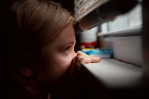 Photo of a little girl peaking through the window blinds for children mental health month