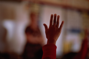 COVID-19 and Our Schools, photo of child's hand up in classroom