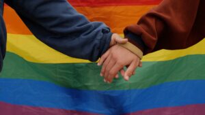 Queer couple holding hands in front of a pride flag