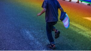 Child running with transgender flag over a rainbow background.