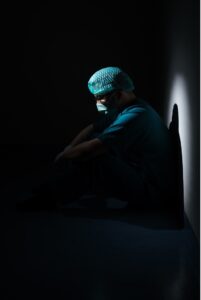 Medical professional in shadow, leaning against a wall.