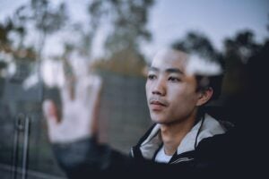 Asian man putting his left hand on clear glass window.