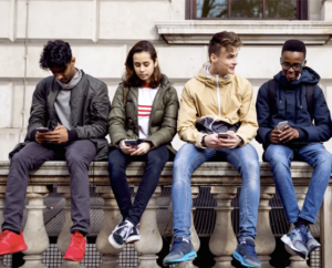 Teens seated side by side looking at phones.