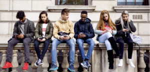 Teens seated side by side looking at phones.