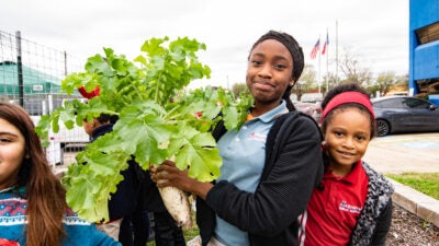 Hunger Action Month - Teenage girl proudly holds up a large radish plant grown from a community garden